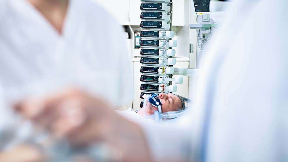 Patient lies in an intensive care unit - there are a lots of  B. Braun infusion pumps in the background