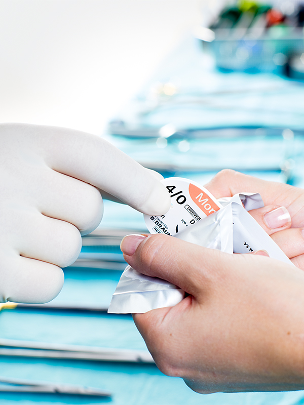 Hand with glove removes suture material from a sterile package