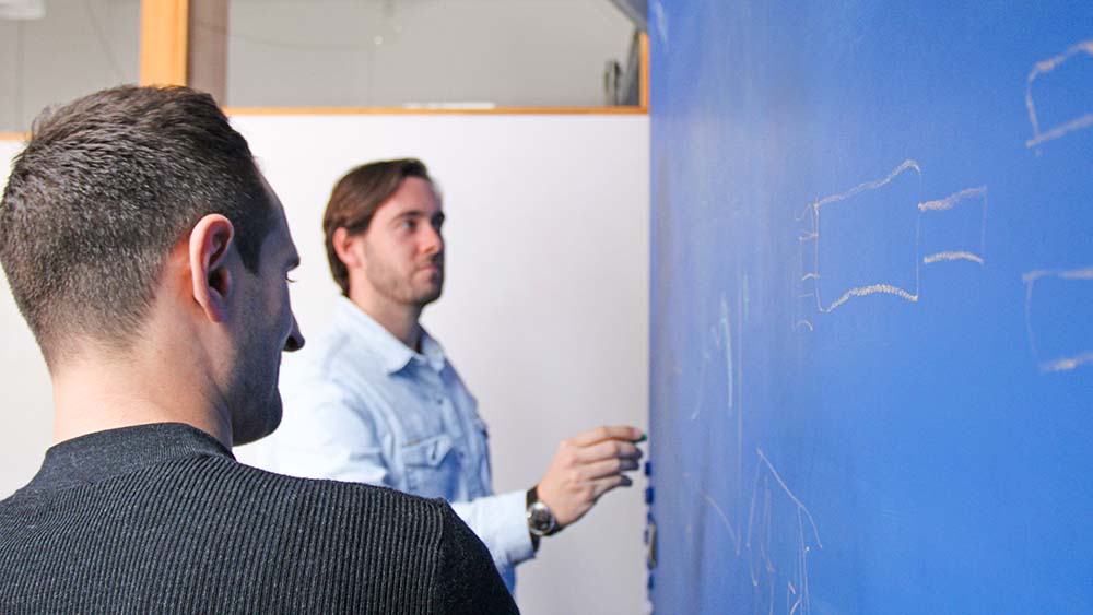 Two men stand at a blueboard and make sketches