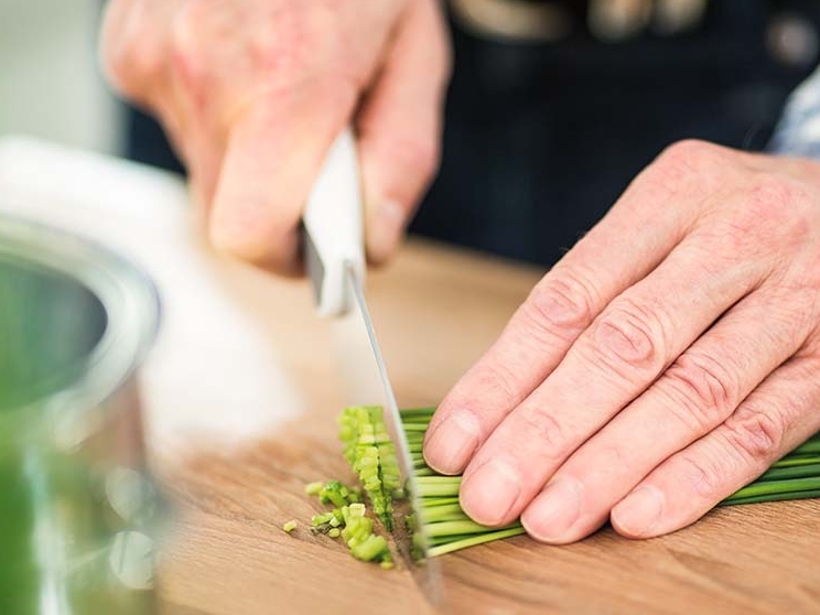 Two hands chop chives on a chopping board