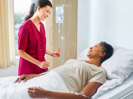 Female nurse administering intravenous solution to a female patient lying in  a hospital bed