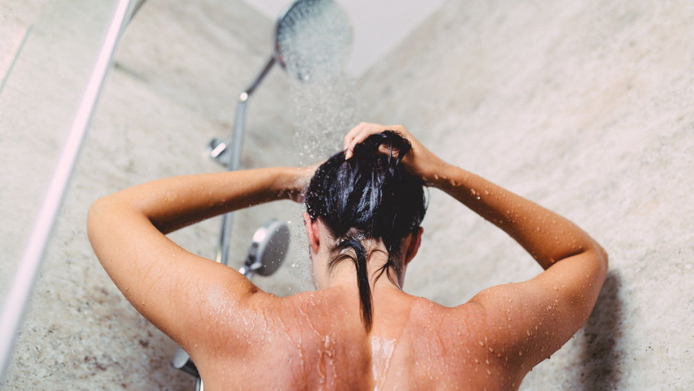 A woman is standing in the shower with the water running
