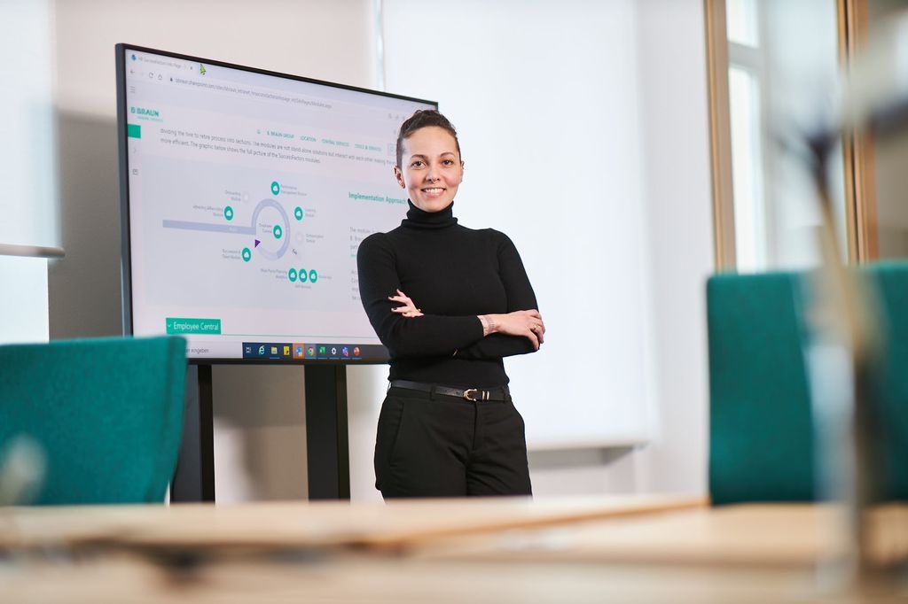 B. Renata Almeida, a Braun employee, standing and grinning in front of a TV that displays graphs at an office. 