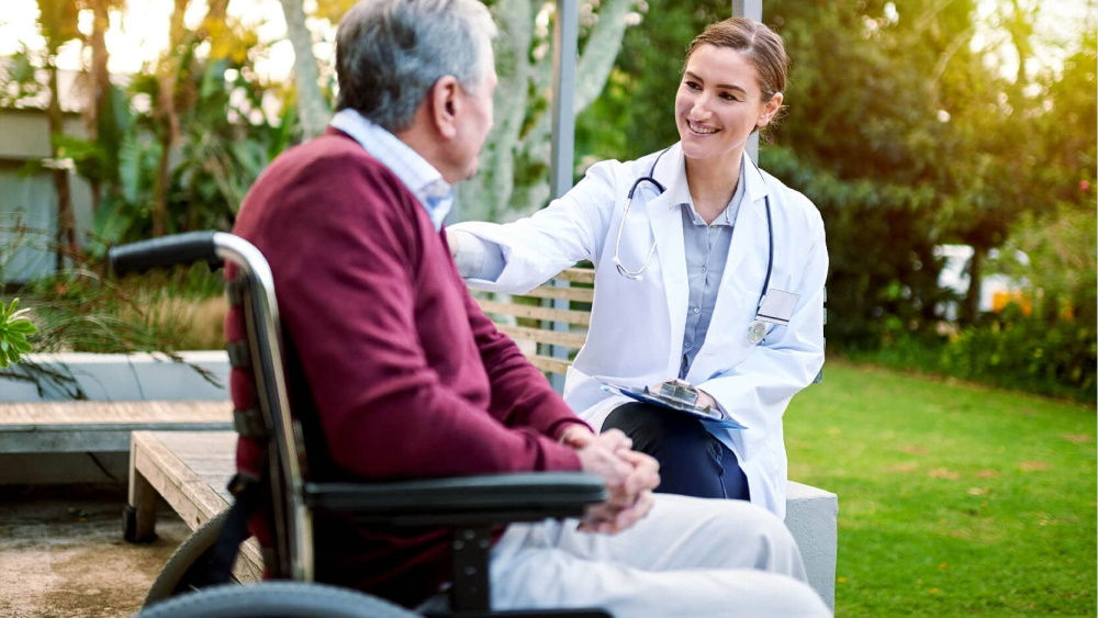 nurse with man in wheelchair outside in the garden