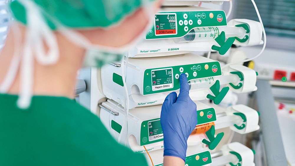 Healthcare professional adjusting infusion pump settings beside a patient care workstation.