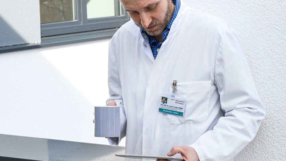 A male doctor holds a cup of coffee and works with his tablet