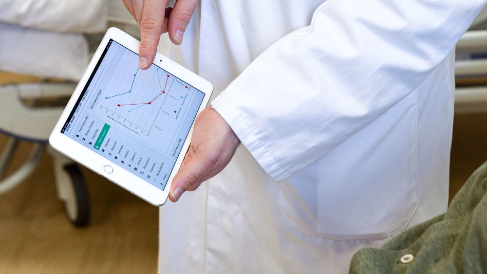 Hands of a medical worker holding a tablet with NEXADIA® mobile companion open and showing statistical data