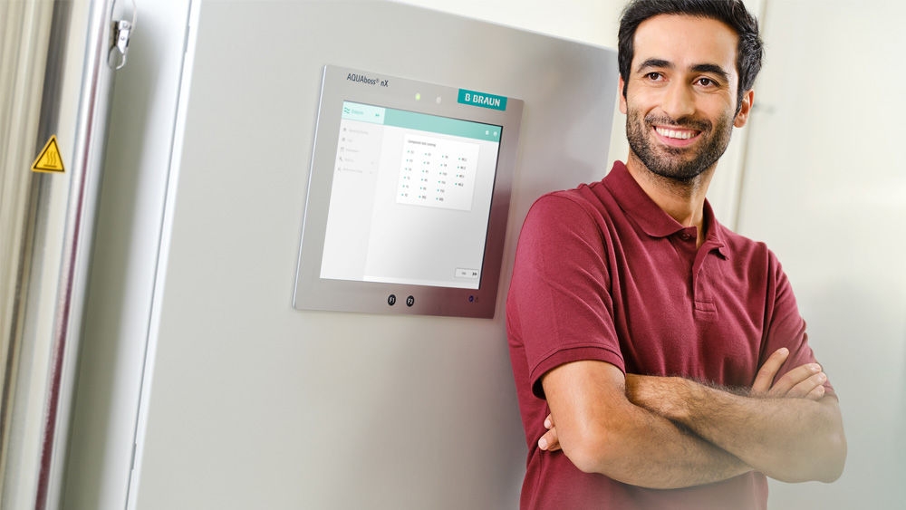 A technician in a red polo shirt standing infront of a water treament system, AQUAboss nX.