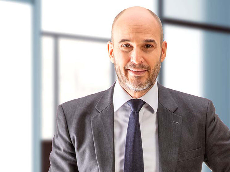 A man in a suit and tie smiles straight into the camera