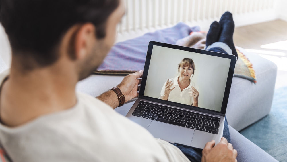 Person sitting on a couch using a laptop for a video consultation with a healthcare professional.