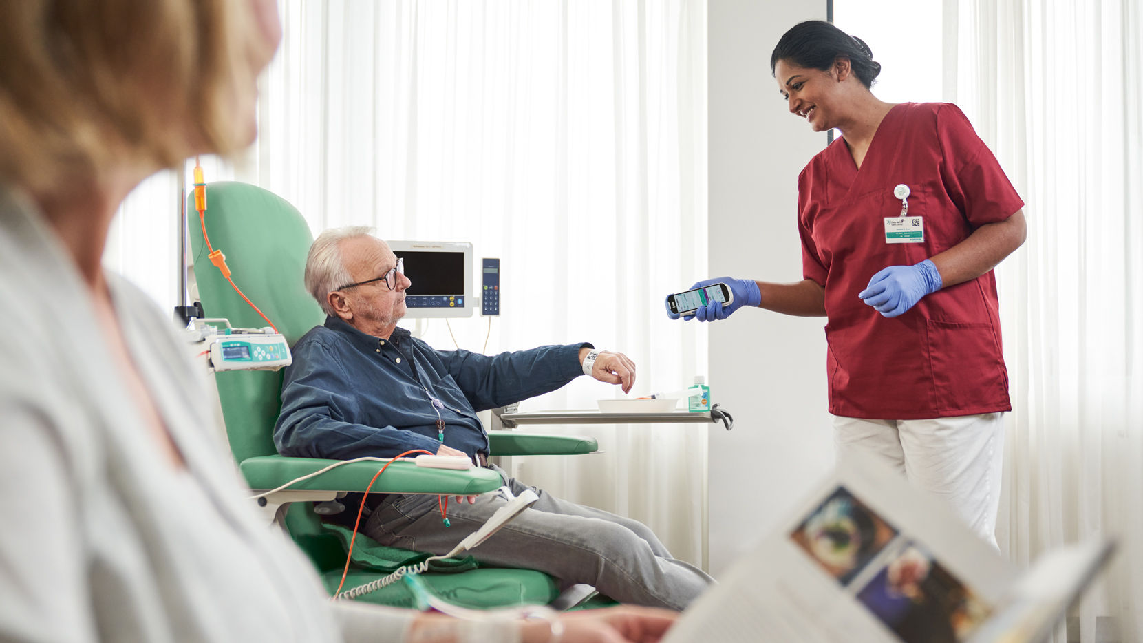 Oncology patient with glasses sitting on the chair and nurse with gloves scanning patient identification on wristband for safety and documentation 