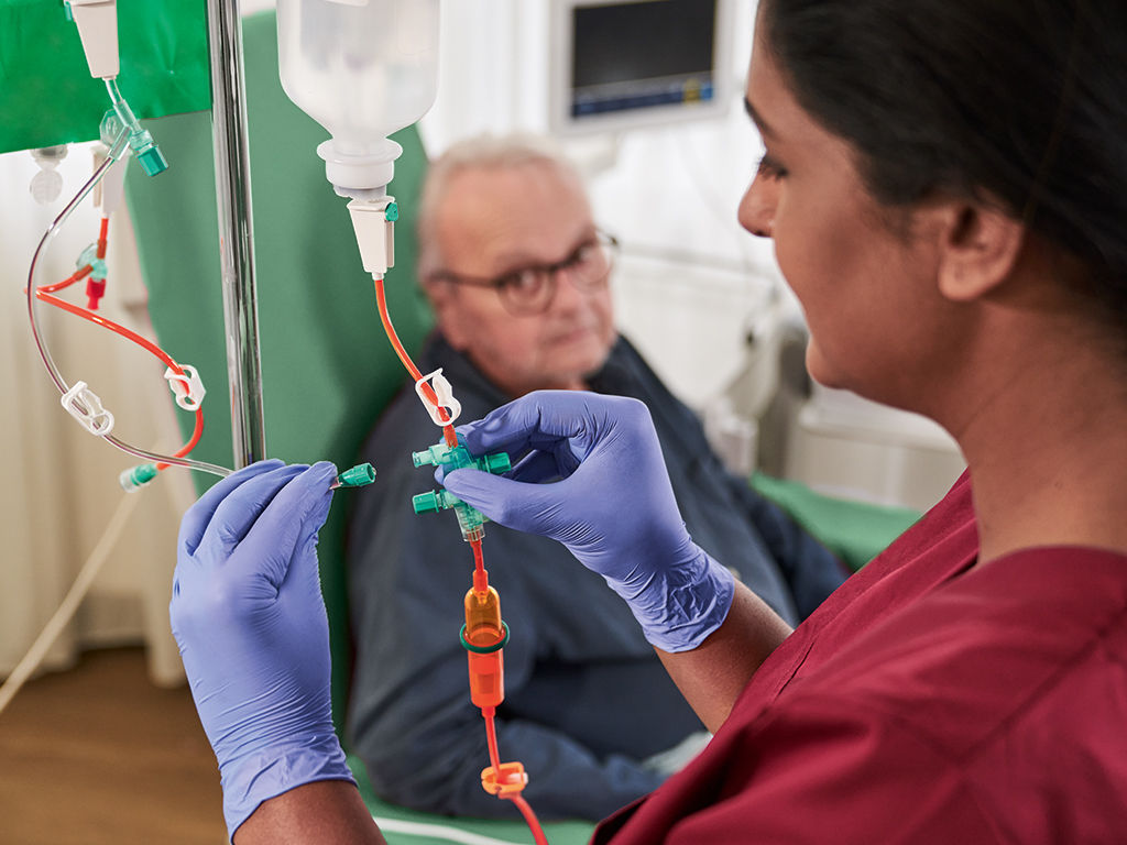 Oncology patient with glasses sitting on the chair and nurse with gloves handling cytoset 