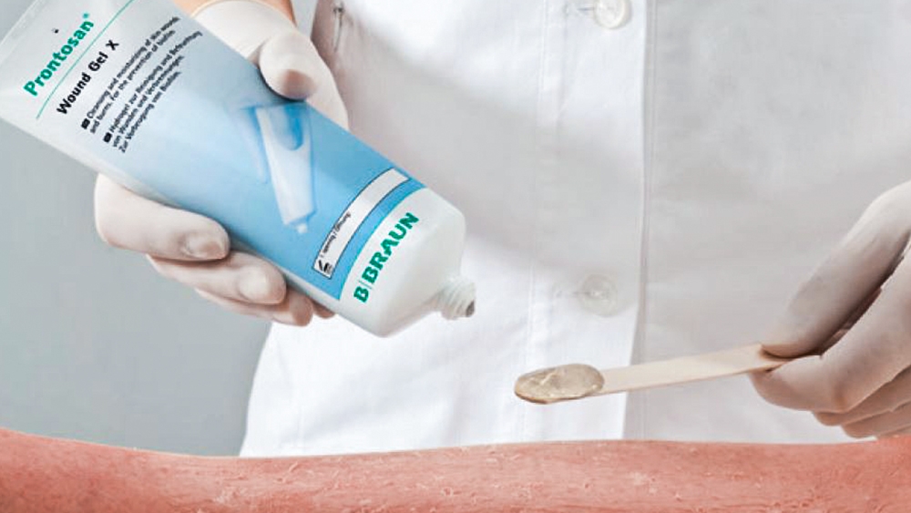 A close-up of a gloved hand holding a prontosan paste and applying the gel to a burn wound