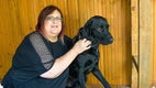 Vera sitting on a wooden bench with her black dog