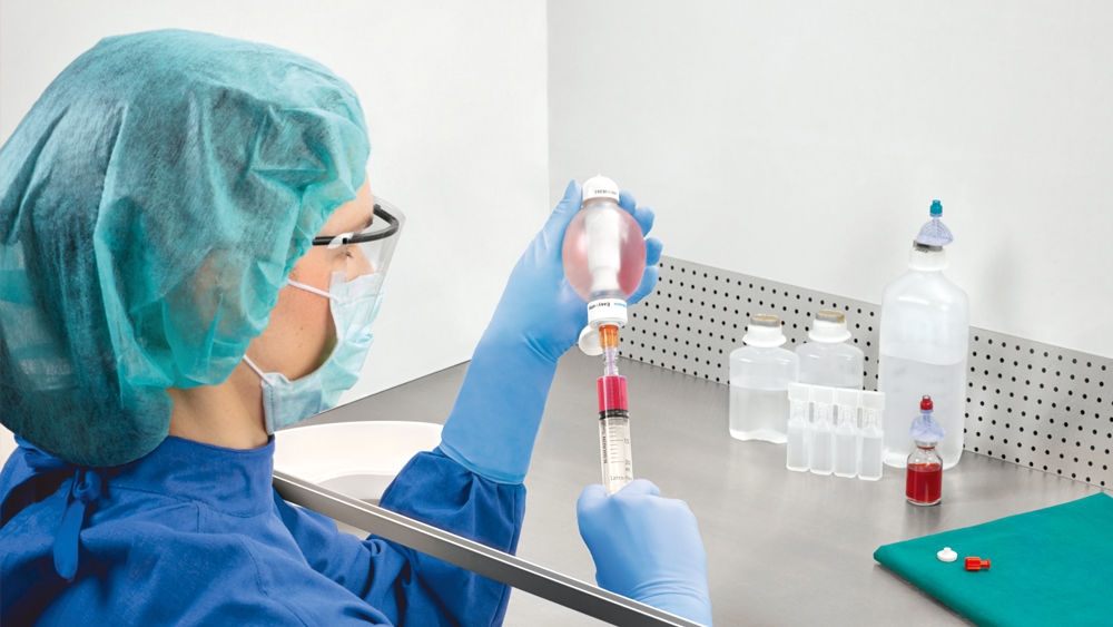 A healthcare professional draws red liquid from a bottle using a syringe