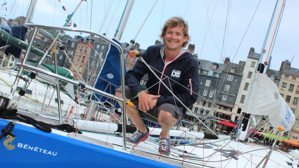 A man sits smiling on a boat, in the background are houses