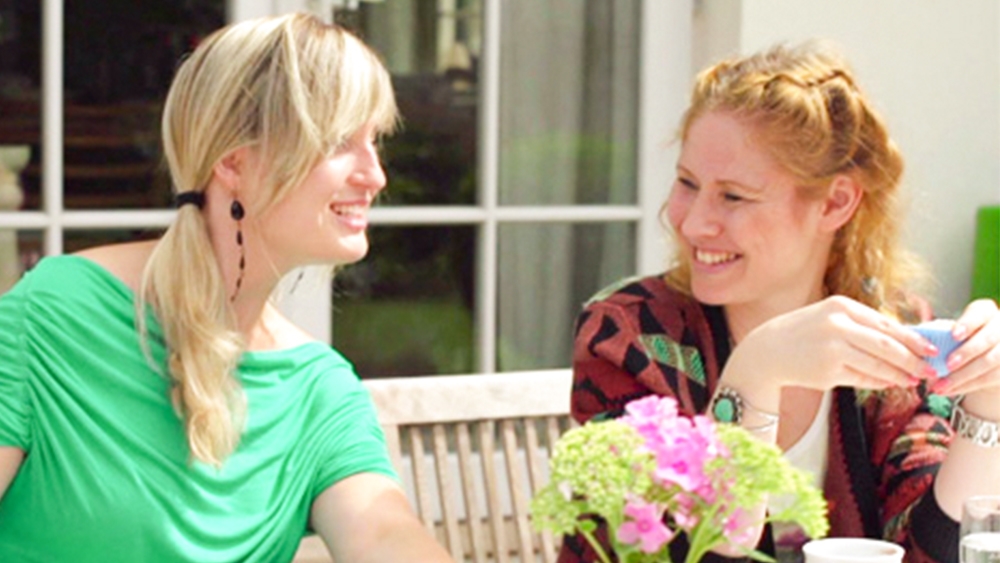 Two young women sit at the table laughing and having a coffee