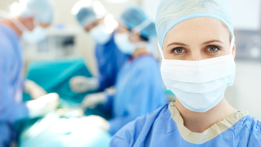 In the foreground is a female surgeon, in the background are three other surgeons during an operation