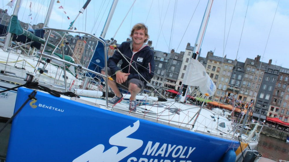 A man is sitting with a smile on a yacht, with a port in the background