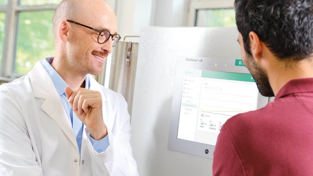 A nephrologist in a white lab coat with a technician infront of a water treatment system AQUAboss nX.