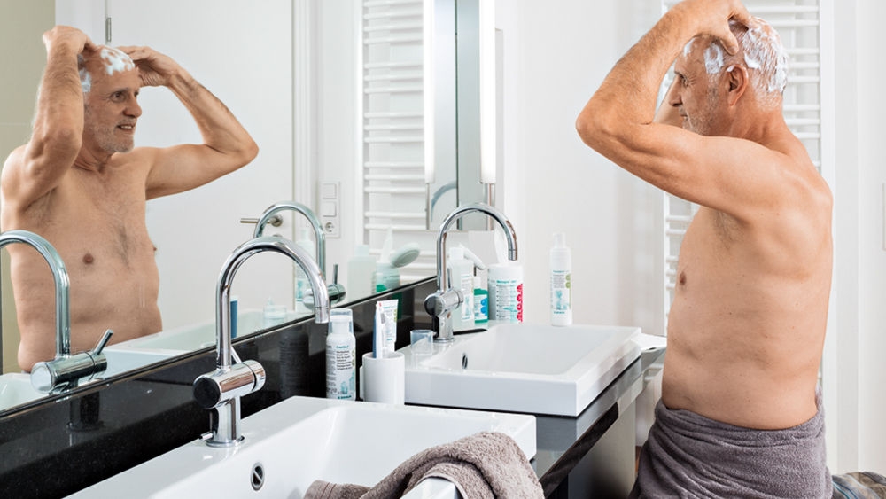 Elderly man in front of mirror in privat bath room performing hear and head decolonization.