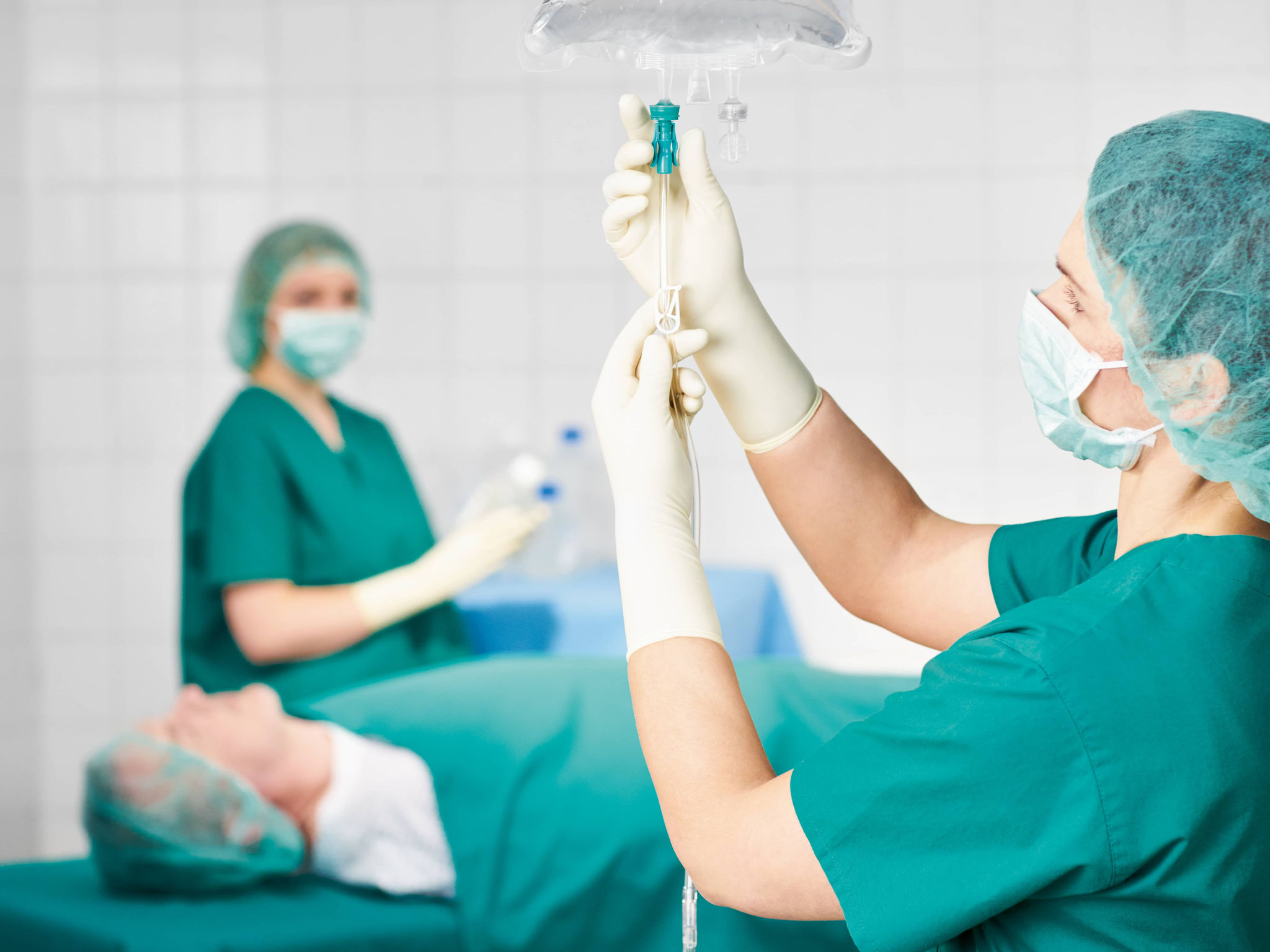 Nurse preparing 3 chamber bag in an operating room - patient lying in the background