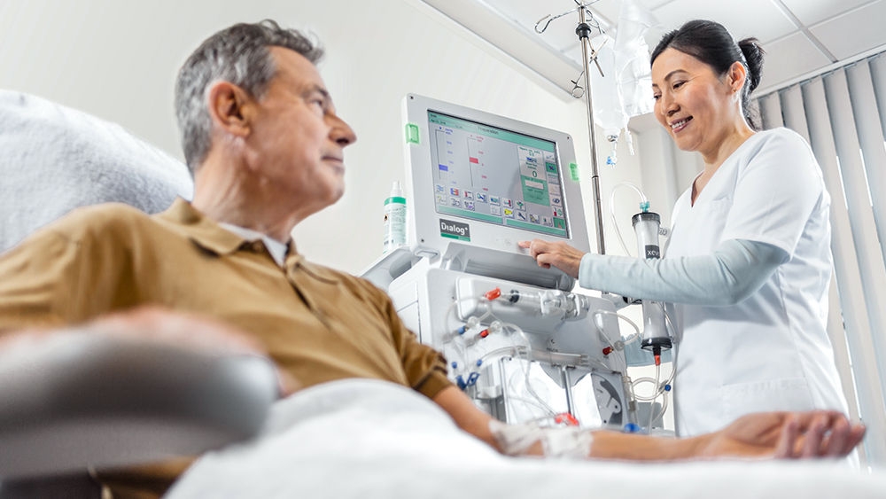 Patient gets dialysis, in the background a nurse handling a dialog + machine