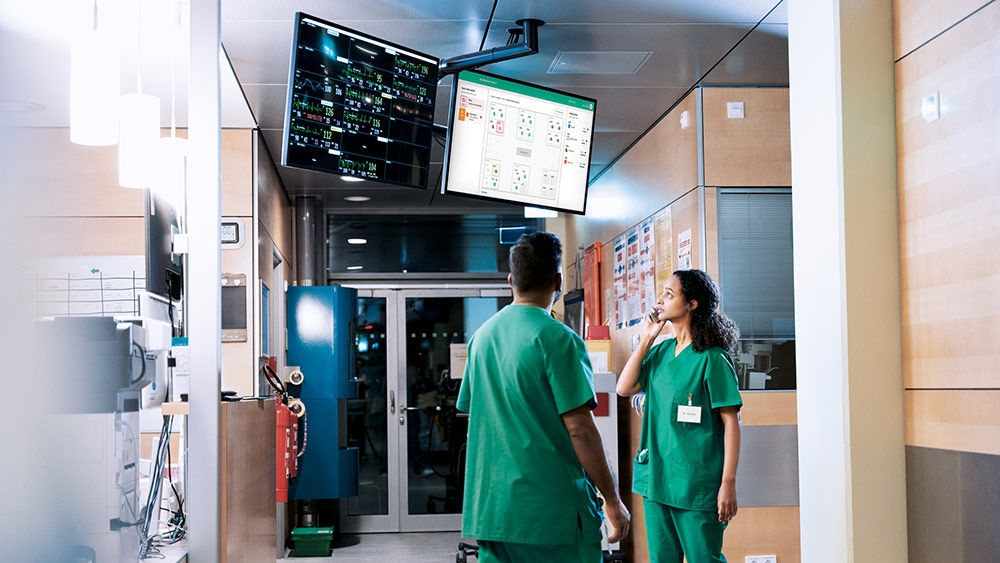 Two healthcare professionals viewing patient and operational information on hospital monitoring displays