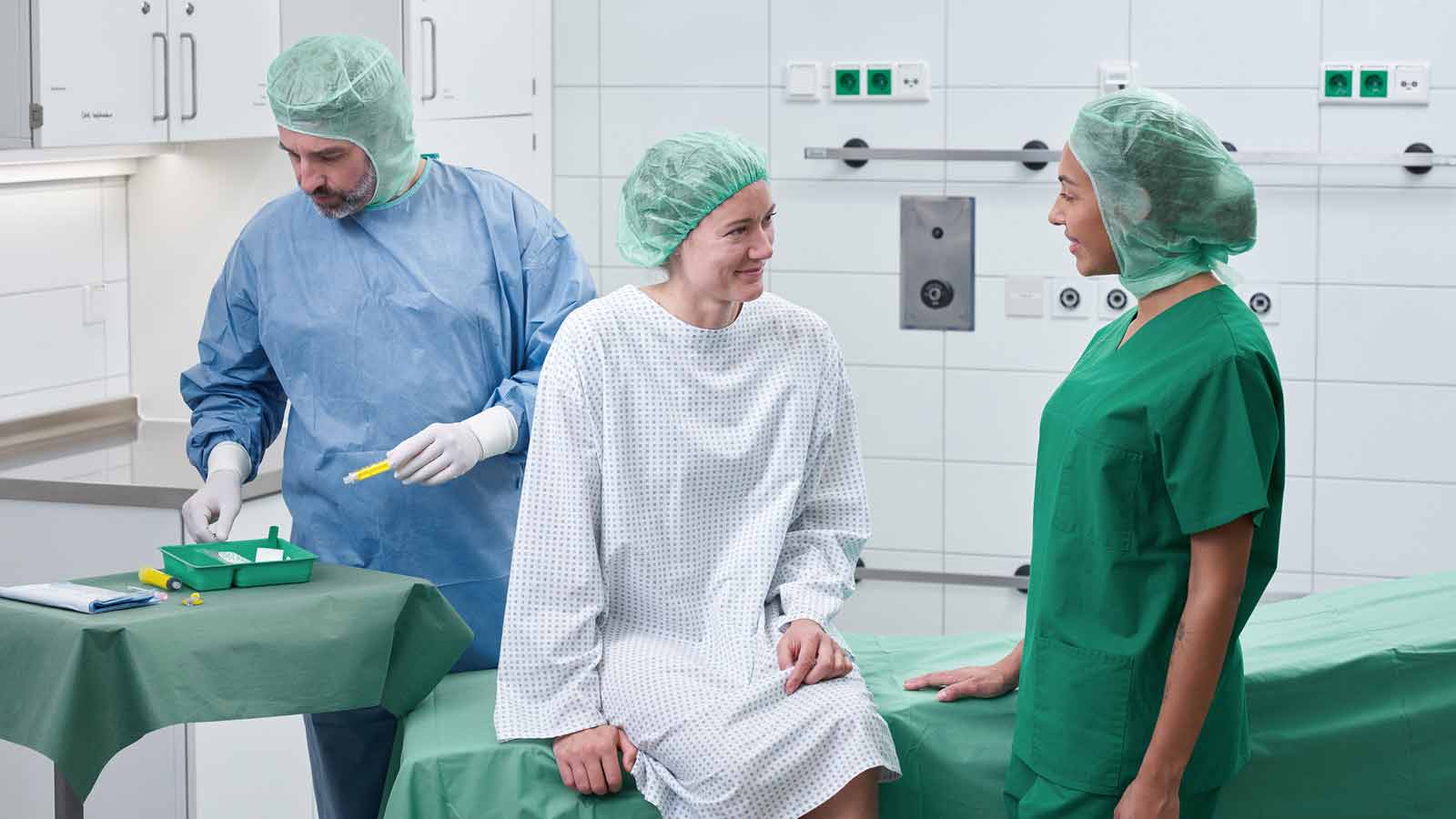 Hospital room with medical equipment, showing a patient bed, monitoring devices, and clinical supplies. A health care professional in medical clothing is preparing for patient care.