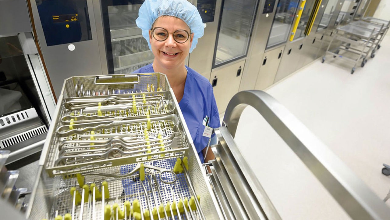 A nurse stands smiling next to a shelf with a set of instruments