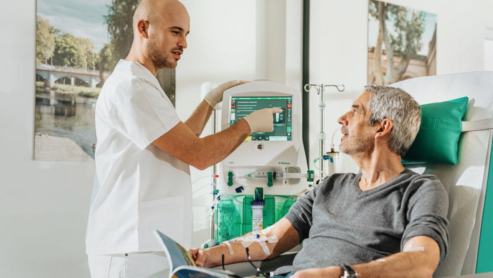 A patient undergoing an apheresis treatment while a healthcare professional explains treatment information using the apheresis system display.​
