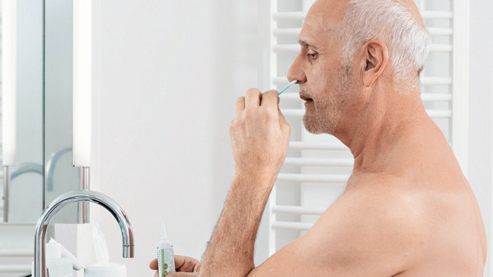 elderly man performing  antimicrobial nose rinsing at home in front of bath mirror 