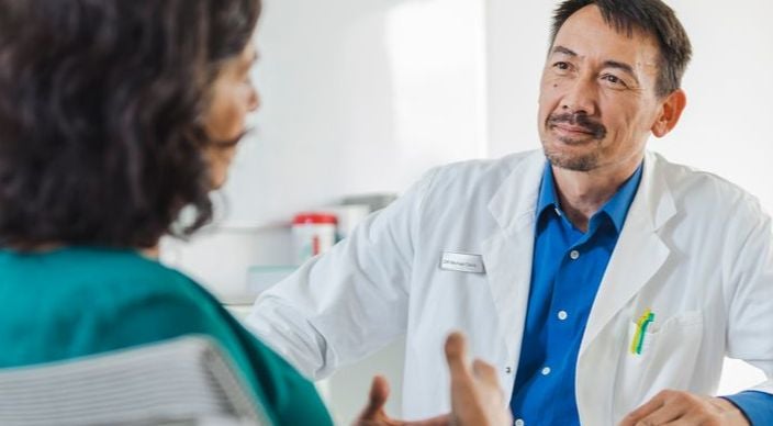 Male doctor with woman in conversation, sitting at a table opposite. 
