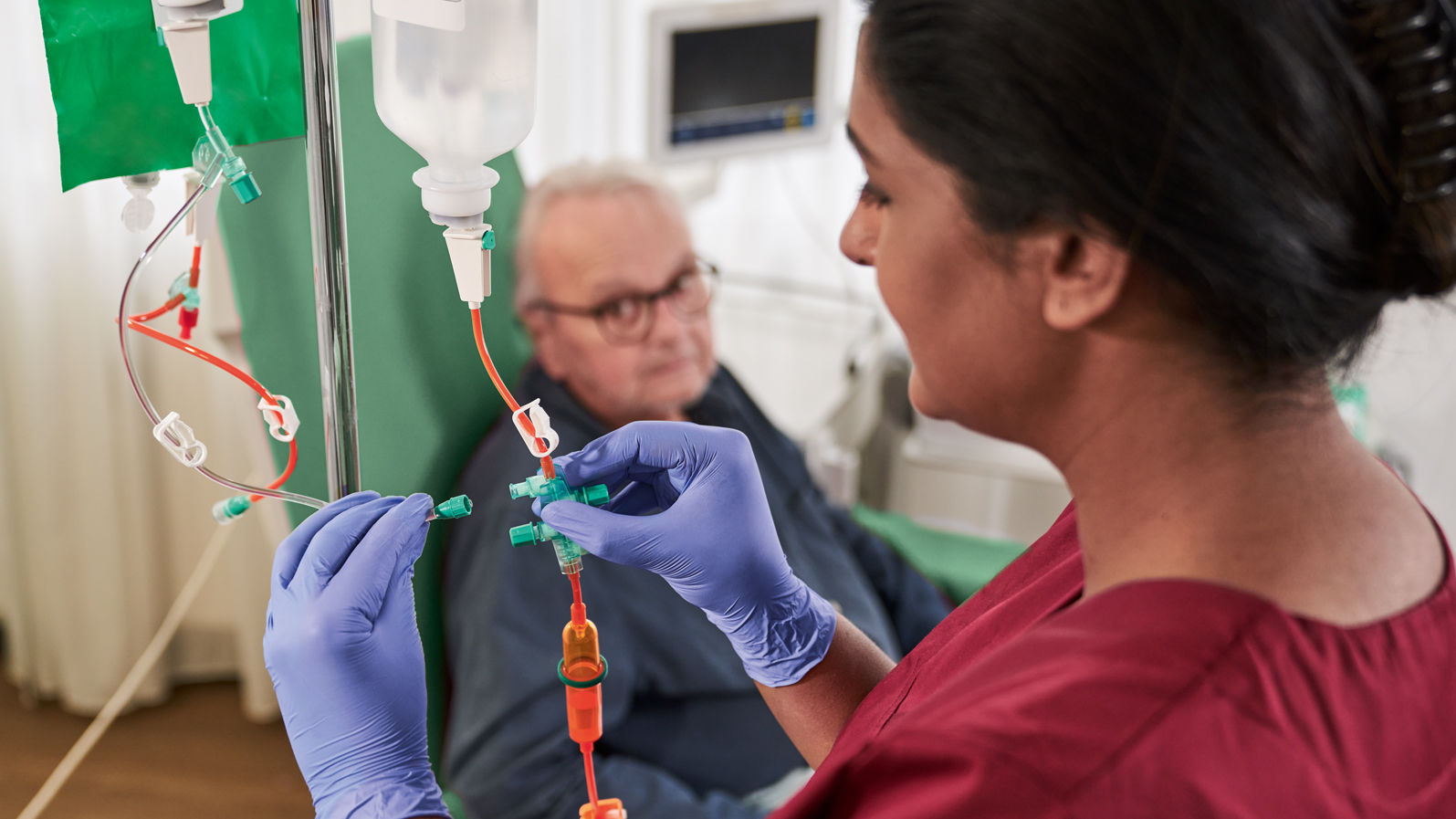 Oncology patient with glasses sitting on the chair and nurse with gloves handling cytoset 