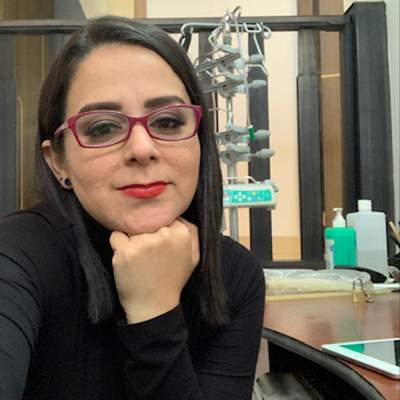 woman with dark hair, glasses and lipstick rests head on her hand