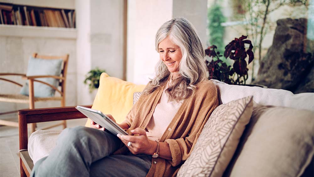 A woman sits on a sofa and reads on her tablet