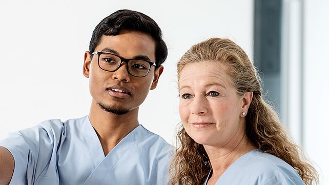 A male and a female nurse stand next to each other and watch something together