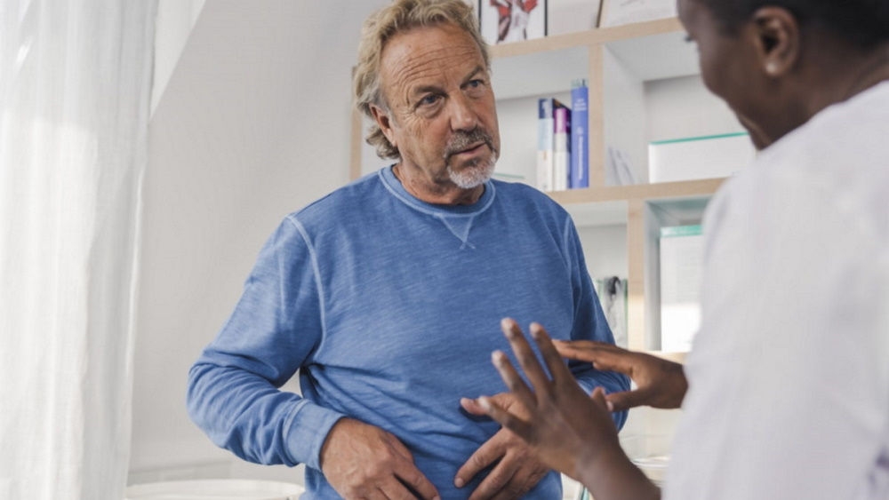 Man talking to nurse, with hands on right side of abdomen