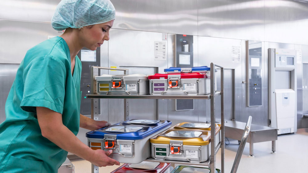 A female healthcare professional, dressed in green scrubs, stands in a clinical setting, holding one of the displayed medical containers