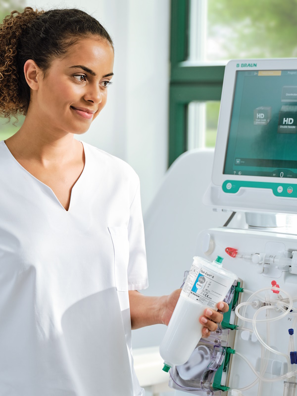 Dialysis nurse stands beside a dialysis machine Dialog iQ, holding a bicarbonate cartridge Sol-Cart B.