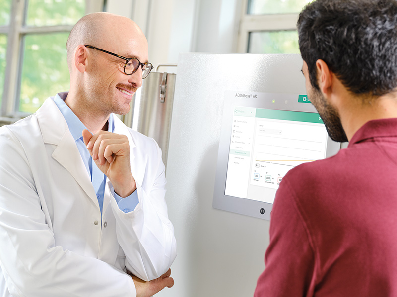 Nephrologist in a lab coat with technician standing in front of a water treatment system AQUAboss nX.