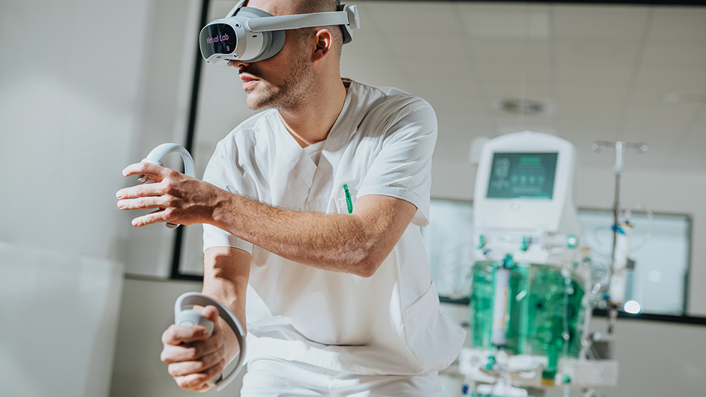 A dialysis nurse wearing a VR headset and holding controllers, with the OMNI plus in the background.​