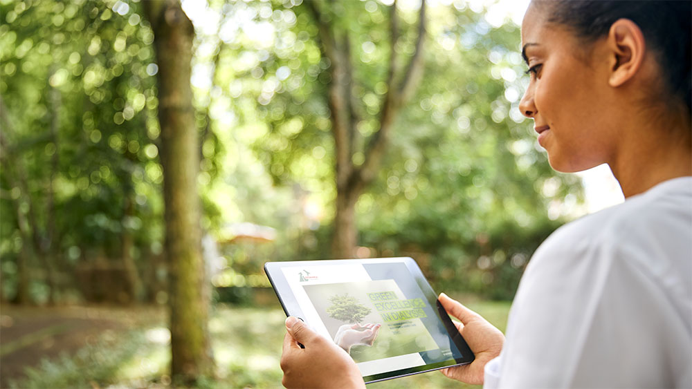 A dialysis nurse standing in a park while viewing a booklet on an iPad.​