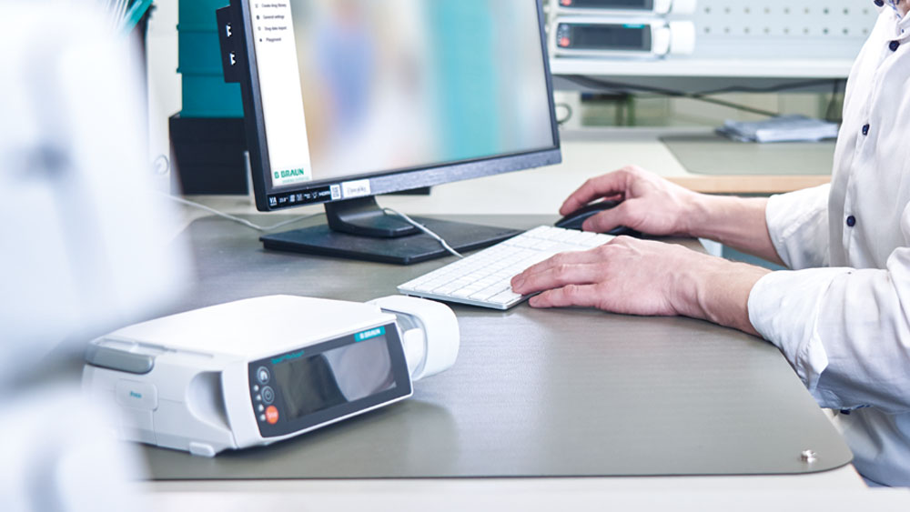 Biomed sits in front of his computer. In the foreground is a B. Braun infusion pump.