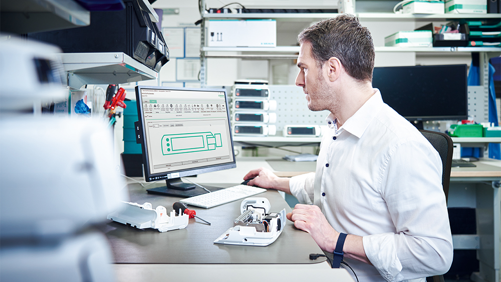 Biomed sits in front of his computer and repairs an infusion pump