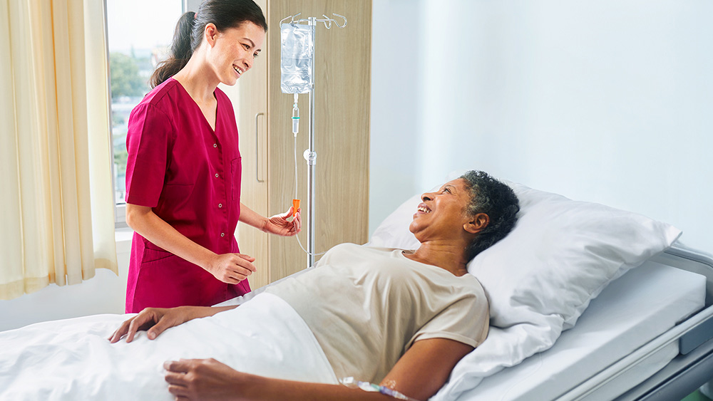 Female nurse administering intravenous solution to a female patient laying in a hospital bed