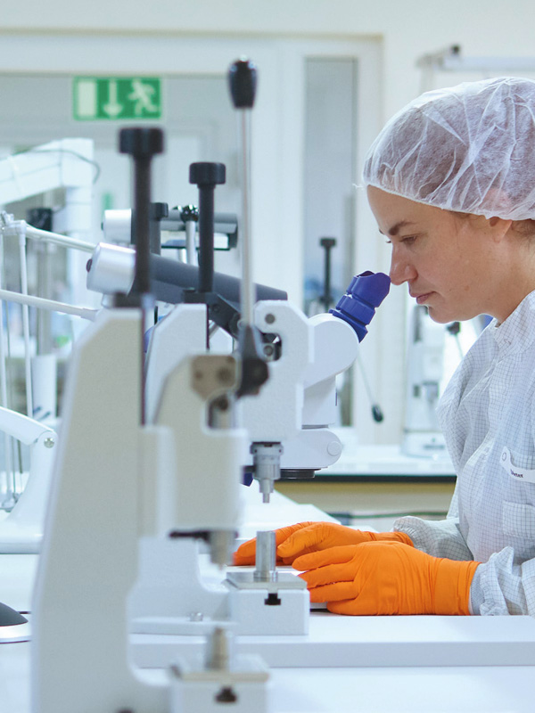 A female healthcare professional sits at a table, analyzing samples through a medical microscope