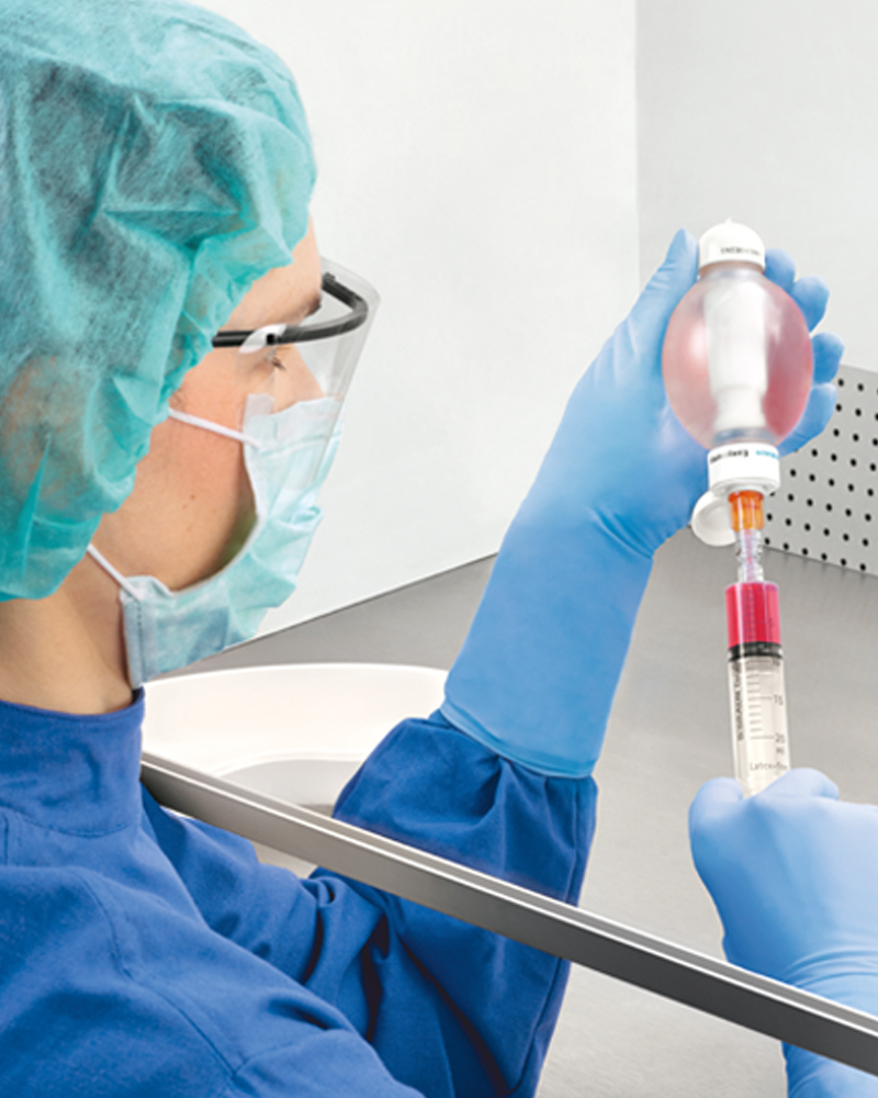 A healthcare professional draws red liquid from a bottle using a syringe