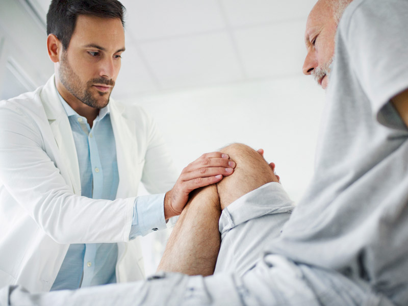 The patient is seated on an examination table, and the healthcare professional is gently examining the knee, possibly assessing for pain or mobility issues