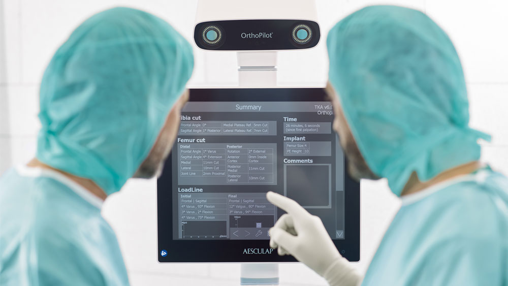 Two doctors in coats and gloves look at the ortopilot elite, a doctor points at the screen.